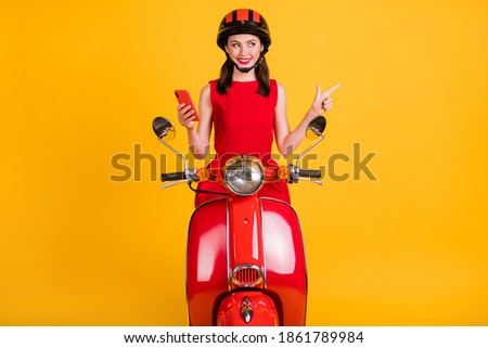 Photo of cute woman dressed red outfit riding vintage moped holding modern device pointing empty space isolated yellow color background