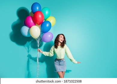 Photo of cute young girl hold many balloons look up empty space wear green sweater short denim skirt isolated blue color background