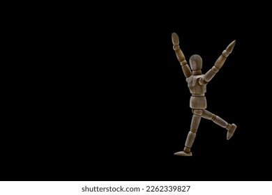 Photo of a dark colored wooden mannequin with neutral black background, it is in motion, with arms open and stretched upwards. Photo to be able to cut out. Concepts. Selective focus. Space for copy