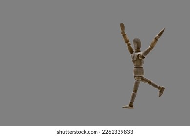 Photo of a dark colored wooden mannequin with neutral gray background, it is in motion, with arms open and stretched upwards. Photo to be able to cut out. Concepts. Selective focus. Space for copy
