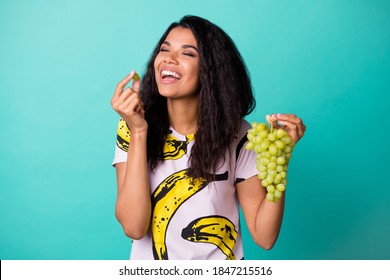 Photo of dark skin girl enjoy eat ecological grape wear pink t-shirt isolated over teal color background