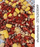 The photo depicts a classic Louisiana crawfish boil, a traditional Cajun meal. A large pile of vibrant red crawfish is surrounded by corn on the cob, potatoes, and sausage.