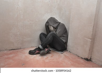 Photo of desperate young drug addict wearing hood and sitting alone in corner. - Shutterstock ID 1058954162