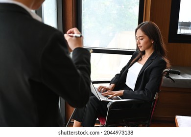 Photo Of A Disabled Woman Using A Laptop Computer While Seated In A Wheelchair With A Conference Room As A Background.