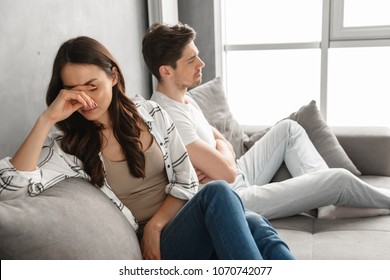 Photo of disappointed couple sitting together on sofa at home with upset look and expressing quarrel isolated over white background