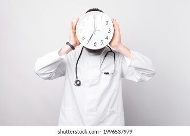 Photo Of Doctor With Clock In Front Of Face As Sign Of Time Pressure. Isolated On White Background