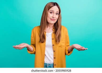 Photo Of Doubtful Unsure Young Woman Dressed Yellow Shirt Smiling Compare Arms Empty Space Isolated Teal Color Background