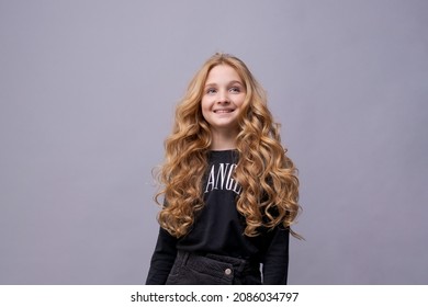 Photo of dreamy cute positive little girl with blond long wavy hair looking blank space wonder smile in black clothes isolated on light gray background