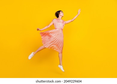 Photo Of Dreamy Girl Jump Hand Catch Empty Space Wear Striped Dress Sneakers Isolated Yellow Color Background