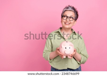 Photo of dreamy pensioner business lady khaki trendy shirt hold piggy bank look empty space earn money isolated on pink color background