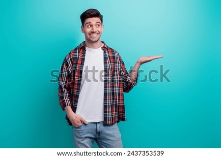Photo of dreamy positive man dressed plaid shirt looking holding arm empty space isolated turquoise blue color background