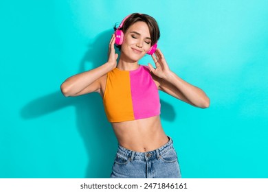Foto de la mujer bonita de ensueño que lleva la parte superior naranja rosa ojos cerrados disfrutando de la música auriculares aislados color verde azulado de fondo Foto de stock