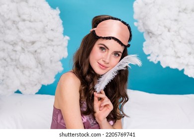 Photo of dreamy shiny woman dressed pink pajama fluffy feather touching cheek sitting bed isolated blue color background - Shutterstock ID 2205769741