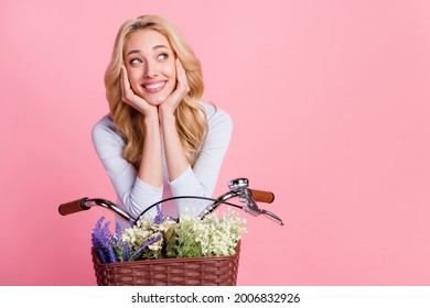 Photo of dreamy young woman look empty space smile hands face bike isolated on pink color background