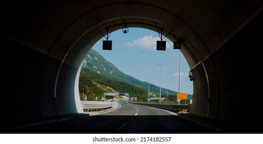 Photo of driving through a dark tunnel on a mountain highway with a view of the light at the end of the tunnel.