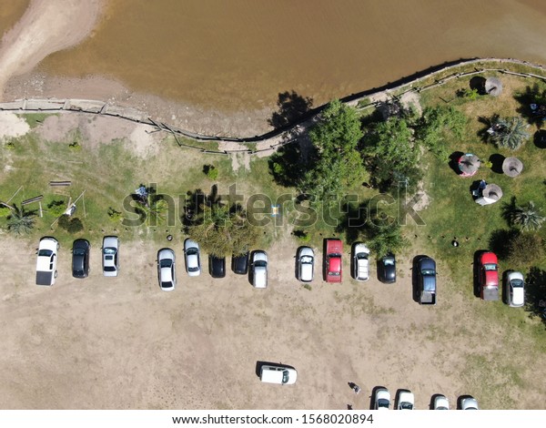Photo from a drone\
with a bird\'s eye view of the coast of a river and parked cars.\
Entre Ríos, Argentina.