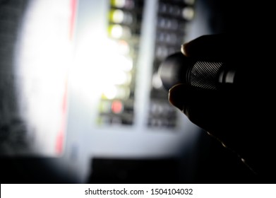 Photo During A Power Outage With Silhouette Of Hand Holding A Flashlight Aimed At A Fuse Box