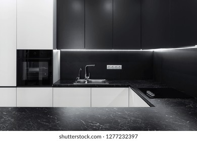 Photo Of Elegance Interior In New Hotel Apartment. Modern Black Kitchen Furniture With Steel Water Tap, Light And Electric Stove On Table