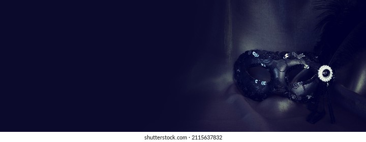 Photo of elegant and delicate black Venetian mask over dark silk background