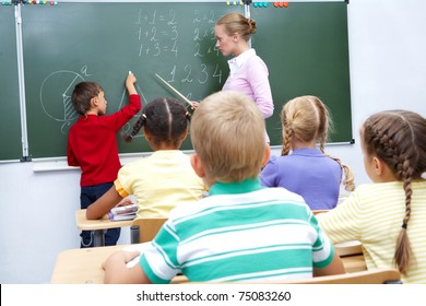 Foto de un estudiante de primaria en la pizarra mirando a su profesor ayudándole