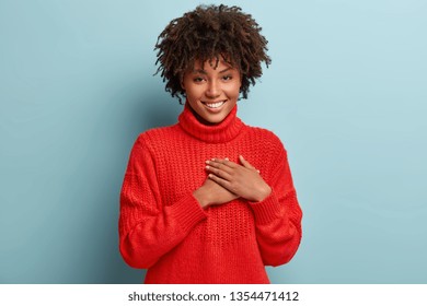 Photo of emotional dark skinned female touches heart with both palms, demonstrates thankful gesture, has good natured expression, expresses great sympathy, gratitude with honesty, feels love - Shutterstock ID 1354471412