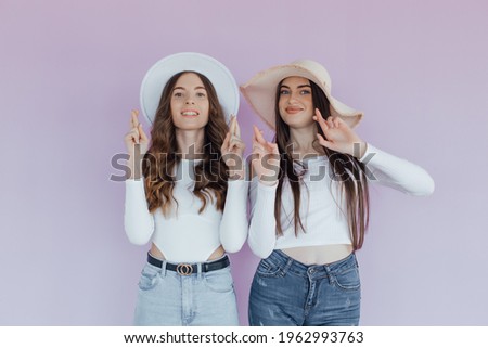 Photo of emotional two women friends standing isolated over purple background. Looking camera showing peace and rock gesture.