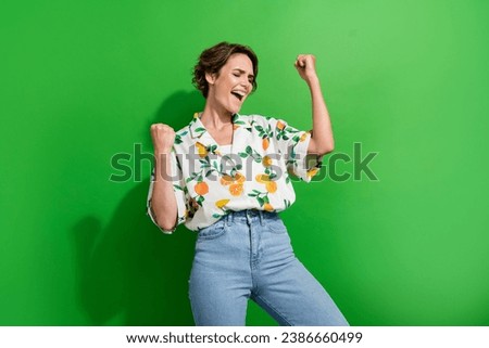 Photo of excited funky lady wear print shirt shouting yes rising fists isolated green color background