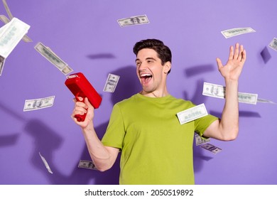 Photo Of Excited Funky Young Man Guy Wear Green T-shirt Shooting Money Gun Smiling Isolated Violet Color Background