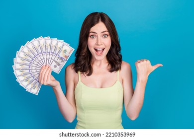 Photo Of Excited Funny Girl Dressed Green Clothes Holding Money Fan Pointing Thumb Empty Space Isolated Blue Color Background