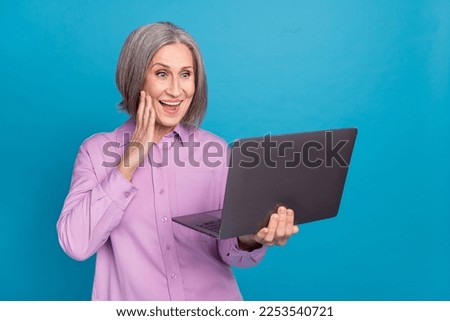 Photo of excited surprised old business woman wear purple shirt touch cheek shocked watching video samsung laptop isolated on blue color background