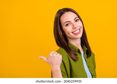 Photo of excited sweet young woman dressed green shirt smiling pointing back finger empty space isolated yellow color background