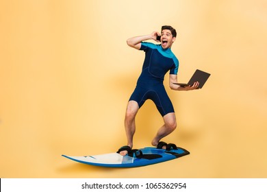 Photo of a excited young man dressed in swimsuit isolated over yellow background on surfing board talking by phone using laptop computer. - Powered by Shutterstock