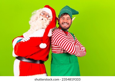 Photo of fat bearded santa claus crossing his arms on green chroma background next to his elf friend. Santa claus and elf with arms crossed