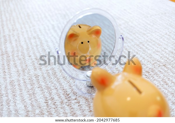 Photo of a fat pink piggy bank looking at\
mirror. Piggy bank in mirror reflection on bright background. A\
pink piggy bank is mirroring himself in front of a elaborate mirror\
design and sees himself.