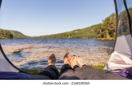 Photo of feet inside of a tent which is located in front of a lake during a summer morning in Scotland
