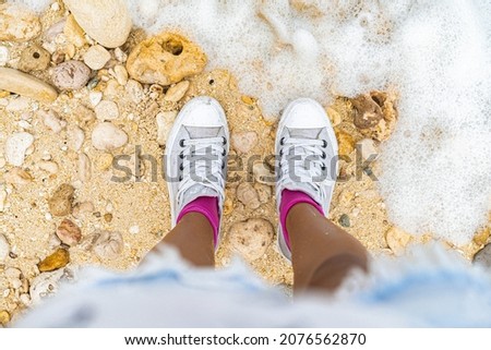 photo of feet in white sneakers on the sand on the shore.