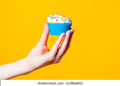 photo of female hand holding cupcake on the wonderful yellow background