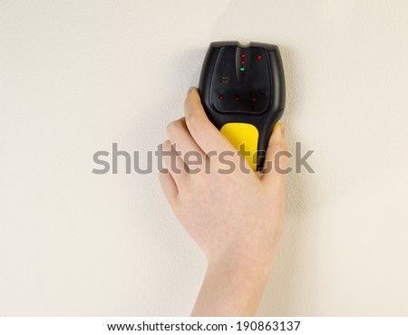 Photo of female hand holding stud finder against interior home white wall