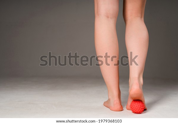 Photo of female\
sports legs. A woman does a foot massage with a red massage ball.\
Isolated on gray\
background