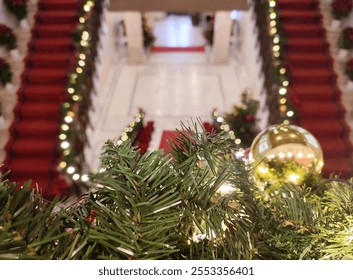 Photo of a festive Christmas decorated City Hall of Athens, featuring a closeup of green garlands, golden ornaments, and bokeh background of Christmas lights decorating the red-carpeted staircases. - Powered by Shutterstock