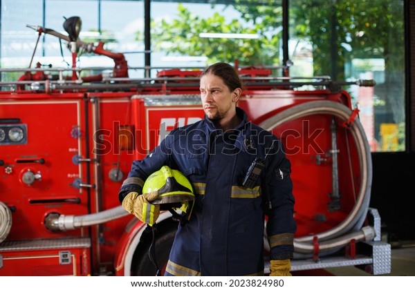 Photo of firefighter man with helmet in her hands\
standing near fire engine