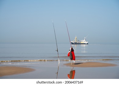 A photo of fishingrods on a dutch beach with a fishing boat in the background.