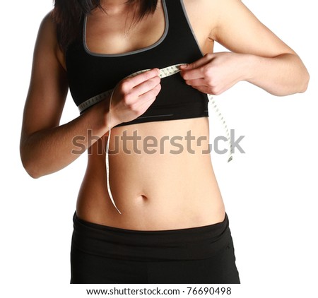 Photo of a fit and healthy young lady measuring her bust with a tape measure in centimeters and millimeters. She has her black gym exercise outfit on. Isolated image on white.