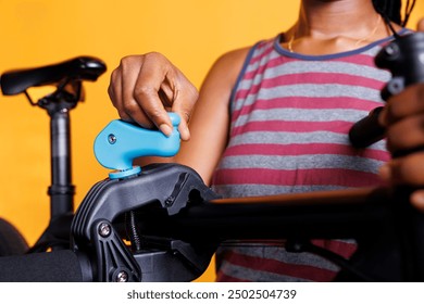 Photo focus of woman adjusting clamp to secure bicycle body on repair-stand for adjustments. Close-up of damaged bike placed on workstand by african american female for maintenance. - Powered by Shutterstock