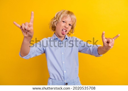 Photo of fooling rude schoolboy wear blue shirt arms showing hard rock sign tongue isolated yellow color background