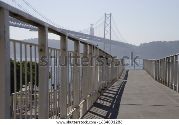 A photo of a foot bridge with the 25 de Abril\
Bridge in the background