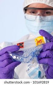 Photo Of A Forensic Lab Technician In Protective Workwear Examining A Plastic Container That Has White Powder In And Is Marked Biohazard And Irritant Inside A Police Evidence Bag.