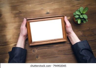 Photo Frame With Copy Space In Male Hands On Wooden Table Background. Business Diploma Or Certificate Mock Up. Family Photo Of A Bored Businessman Template.