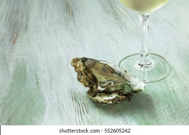 A photo of freshly opened oyster with a fragment of a glass of white wine, on a wooden background texture with copyspace