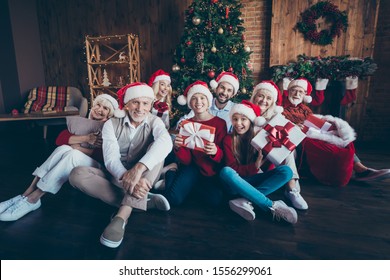 Photo Of Friendly Big Large Family Smiling Toothily Having New Year Party Together Sitting On Floor In Santa Cap Headwear Children In Childhood In Front Of Decorated Tree